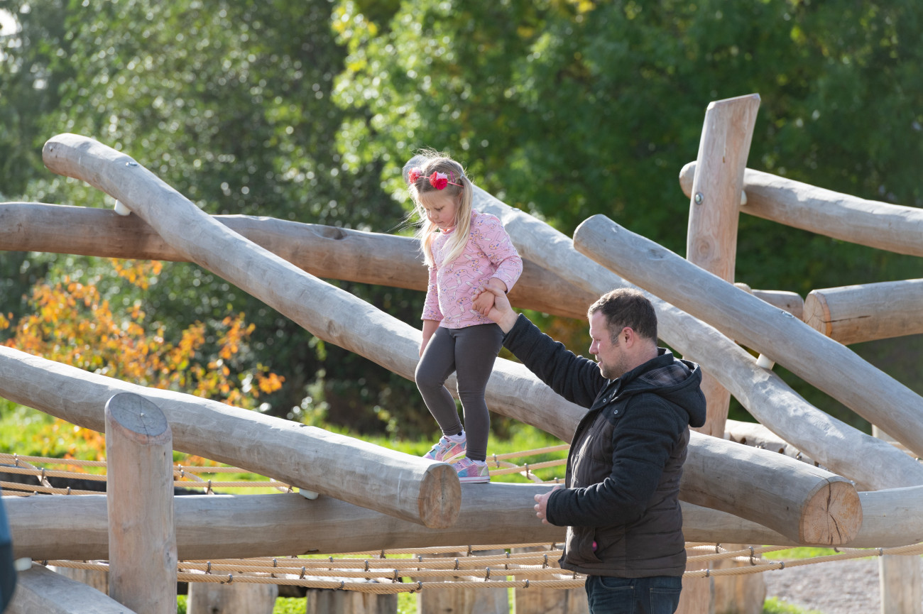 Dad holding his young daughters hand while she walks across wooden beam
