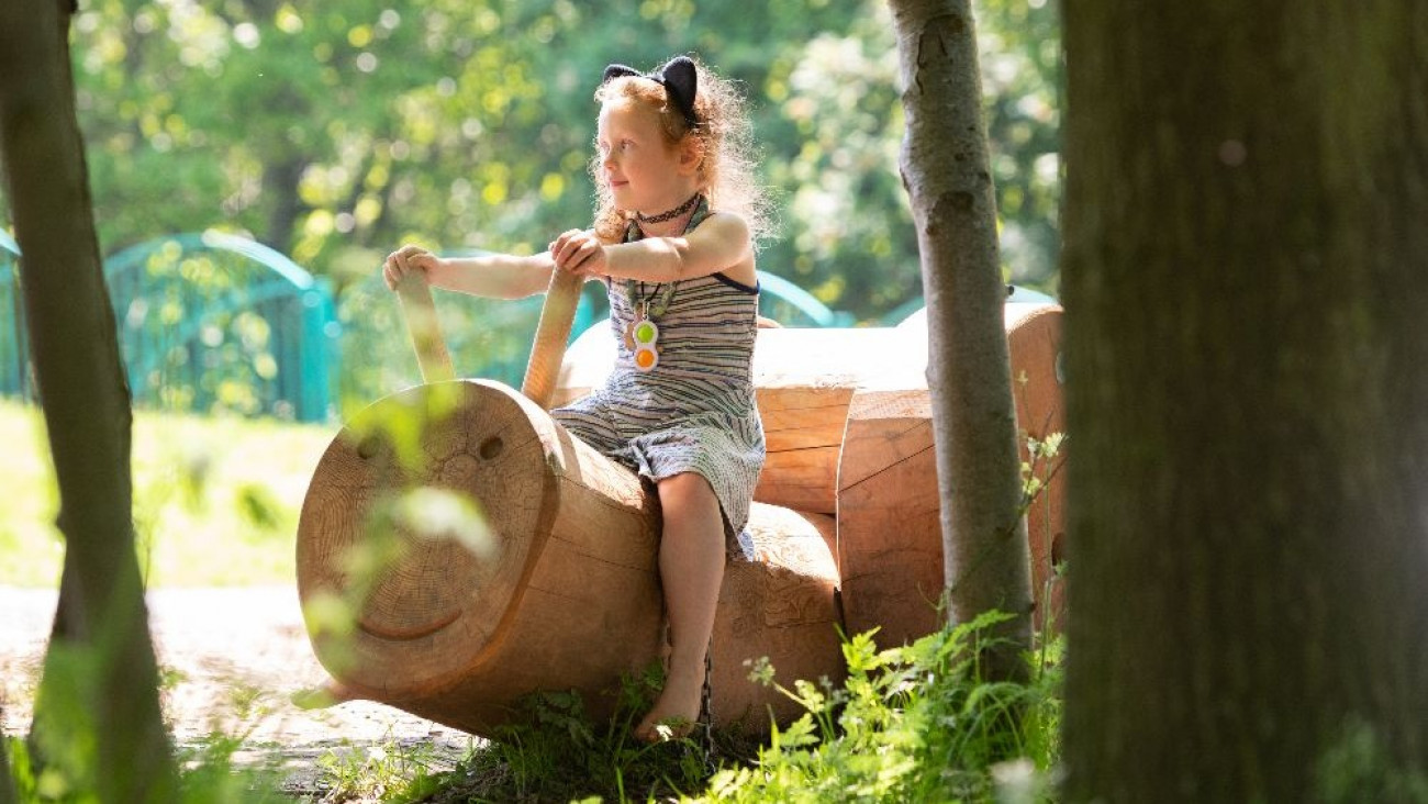 Young girl sitting on a wooden log carved like a caterpillar